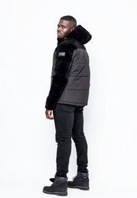 Svart vadderad jacka med övre del i fejkpäls, texturerade ärmar, fickor med dragkedja och huva. Matchas med svarta tajta jeans och stövlar.