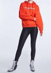 Sudadera roja con el texto "elige la felicidad", combinada con leggings negros y botas tobilleras con un patrón de serpiente y tacón cuadrado.