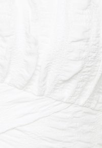 Tessuto bianco testurizzato con leggere pieghe; assomiglia a un materiale leggero e morbido adatto per l'abbigliamento. Nessun motivo o accento visibile.