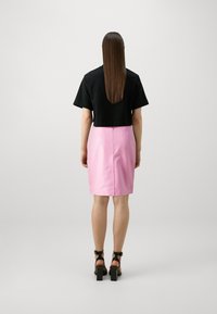 Camiseta negra corta y falda lápiz rosa, con una textura suave y un diseño ajustado. Tacones negros con correas y tacones gruesos.