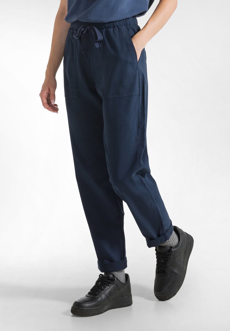 Marineblauwe, elastische broek met een trekkoord, voorzien van zijzakken en opgerolde mouwen, gecombineerd met zwarte sneakers en grijze sokken.