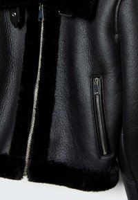 Veste en cuir noir texturé avec des zippers en métal argenté et une doublure en fourrure noire visible le long de la fermeture éclair et de l'ourlet.