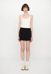 Camiseta sin mangas blanca, pantalones cortos negros con cordones, zapatillas color crema, calcetines blancos. Diseño simple, parte superior ajustada, pantalones cortos relajados, tejido ligero.