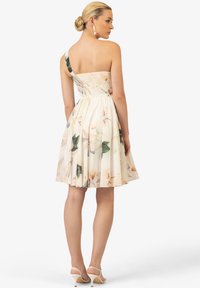 Ein trägerloses Blumenkleid mit gerafftem Oberteil, cremefarbener Stoff und pastellfarbenen Blumenmuster. A-Linien-Rock mit fließender Textur.