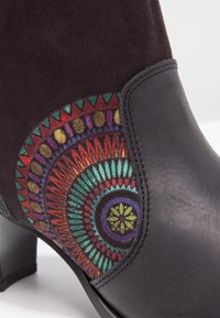 Bottine en cuir et suède noir avec un motif géométrique circulaire coloré sur le côté près du talon et une semelle à talon bloc.
