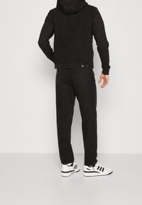 Svart denimjacka med huva, bakvy. Kombinerad med svarta jeans och vita sneakers med svarta ränder. Slät textur, avslappnad design.