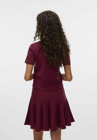 Burgundský dvoudílný outfit, který obsahuje přiléhavý top s krátkými rukávy a rozšířenou sukni s záhyby, vyrobený z měkkého, strukturovaného materiálu.