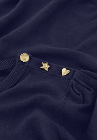 Marineblauwe gebreide kleding met drie decoratieve knopen in goudtint: een bloem, een ster en een hart. Zachte textuur, ronde halslijn en gevouwen ontwerp.