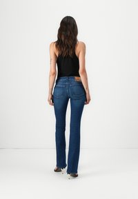 Jean en denim bleu foncé ajusté avec une jambe évasée, design classique à cinq poches, taille haute et une étiquette en cuir à l'arrière.