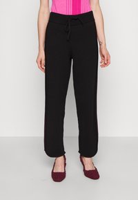 Zwarte gebreide joggingbroek met een taillekoord, voorzien van contraststrepen aan de zijkant in een donkerdere tint, zachte textuur en losse pasvorm.