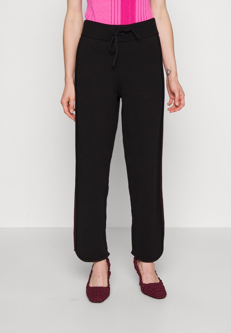Zwarte gebreide joggingbroek met een taillekoord, voorzien van contraststrepen aan de zijkant in een donkerdere tint, zachte textuur en losse pasvorm.