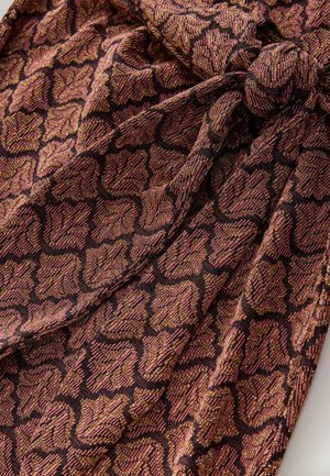 Tyget har ett bladmönster i svarta och koppartoner, med en texturerad, vävd yta. Materialet faller mjukt med en liten lyster.
