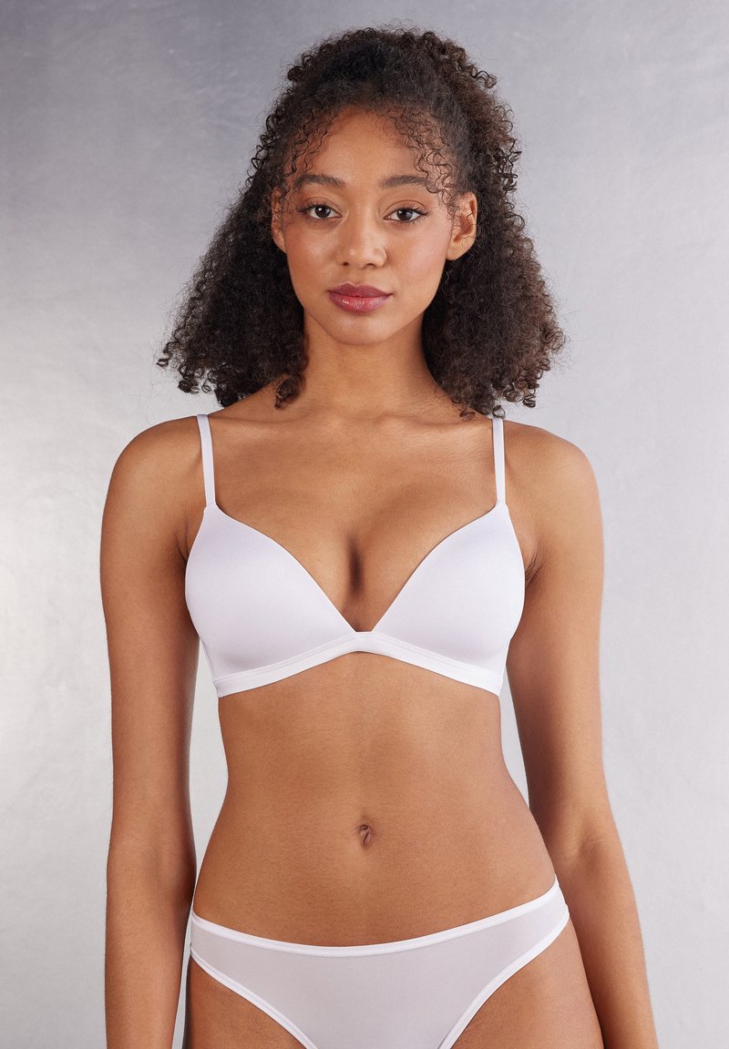 Soutien-gorge sans fil blanc en forme de triangle avec des fines bretelles ajustables, en tissu lisse et aux bords finis. Associé à un slip blanc transparent assorti.