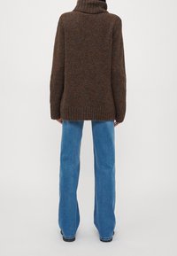 Brauner gestrickter Pullover mit hohem Kragen, lässiger Passform und geripptem Saum, kombiniert mit hellblauen weit geschnittenen Jeans und schwarzen Schuhen.