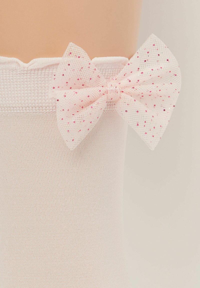 Calzini rosa chiaro con una texture a coste e bordo ondulato, impreziositi da un fiocco trasparente rosa con pois rossi e rosa sul lato.