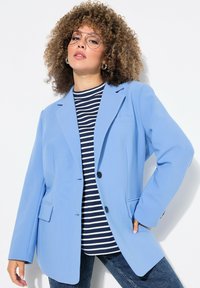Blazer bleu clair à coupe décontractée, avec une fermeture à un bouton et deux poches avant, porté sur une chemise rayée bleu marine et blanche.