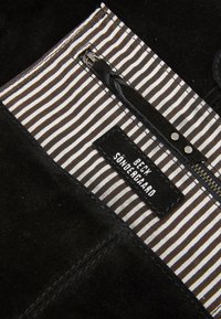 Black suede material features a striped fabric lining in black and white. A zipper with a black pull and a label with white text are visible.