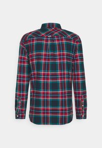 Chemise à manches longues boutonnée, motif à carreaux rouge, vert et bleu marine, vue de dos sur fond blanc.