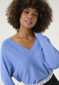 Suéter de pico en azul claro, con cuello y puños de canalé, textura suave y corte holgado, combinado con pantalones negros a rayas.