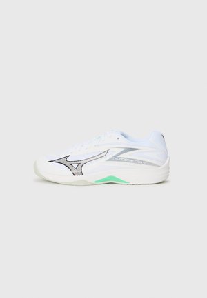 White athletic shoe with a textured upper, silver accents, black graphic design, and a green outsole. Features laces and padded collar.