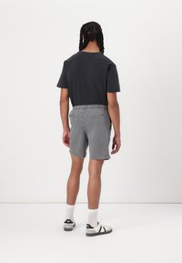 Shorts gris avec une taille élastique et deux poches arrière, associés à un t-shirt noir et des chaussettes blanches avec des baskets noires.