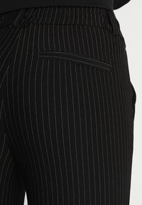 Svarta randiga byxor har ett mjukt tyg, elastisk midja, sidoficka och en skräddarsydd passform med vertikala linjer.