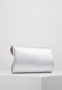 Bolso de mano metálico plateado con textura suave, diseño plegable y bordes redondeados. Apariencia minimalista, sin hardware visible ni patrones.