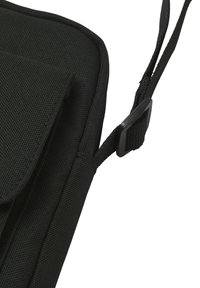 Bolso de hombro de tela negra con una superficie texturizada, que cuenta con un cierre de solapa y una correa ajustable con un hebilla de plástico.