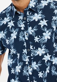 Chemise à manches courtes bleu marine avec un motif floral en bleu clair. Dotée d'une fermeture à boutons sur le devant et d'un col classique. Confectionnée dans un tissu léger.