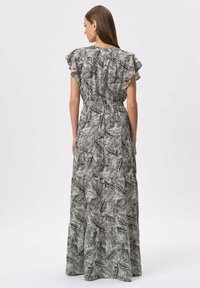 Maxi sukienka w czerni i bieli z motywem liści, krótkimi falbaniastymi rękawami, elastyczną talią i warstwowym dołem. Gładka faktura materiału.