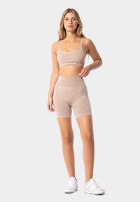 Gaiši bežs sporta krūšturis un atbilstoši augsti vidukļa šorti no mīksta auduma. Ievērojams minimāls zīmols un elegants, pieguļošs dizains.