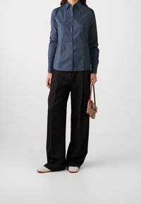 Camicia button-up di colore blu scuro, maniche lunghe, con colletto a punta. Abbinata a pantaloni neri a gamba larga e una piccola borsa a tracolla a fantasia.