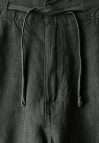 Tummanvihreät pellavashortsit, joissa on naruvyötärö, näkyvät ompeleet ja teksturoitu kangaspinta. Edessä on taskuyksityiskohta.