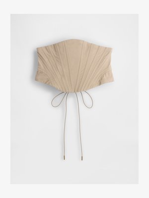 Beženi korzet zgoraj z vertikalnimi gubami, ki ima zožen pas in nastavljive vezi na hrbtu z kovinskimi konicami. Gladka tekstura tkanine.