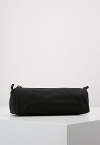 Necessaire cilindrico nero realizzato in tessuto durevole, con chiusura a zip e due alette per un facile accesso. Finitura textured.