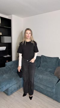 Fekete rövidujjú póló fehér csipkeből készült hosszú ujjakkal rétegezve, magas derekú fekete farmernadrággal és fekete hegyes orrú magassarkú cipővel párosítva.