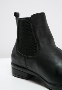 Stivaletto in pelle nera con pannello elastico laterale, texture liscia, punta rotonda, tacco a blocco basso e linguetta per una facile calzata.