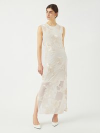 Robe maxi sans manches en tissu blanc transparent, avec une broderie florale beige complexe et des fentes sur les côtés. Assortie à des talons blancs pointus.