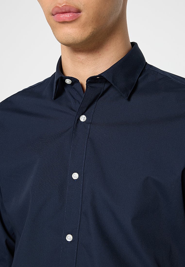 Camicia abbottonata blu navy con colletto alla francese, realizzata in tessuto liscio. Presenta bottoni bianchi e cuciture pulite senza motivi visibili.