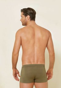 Olivgrön boxerkalsonger med en mjuk textur och en enkel elastisk midjeband, sedd bakifrån, vilket framhäver den minimalistiska designen.