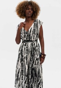 Zwart-wit geprinte jurk met een V-hals, cap sleeves en een taille met ceintuur. Heeft een vloeiende silhoeet en een gladde stoftextuur.