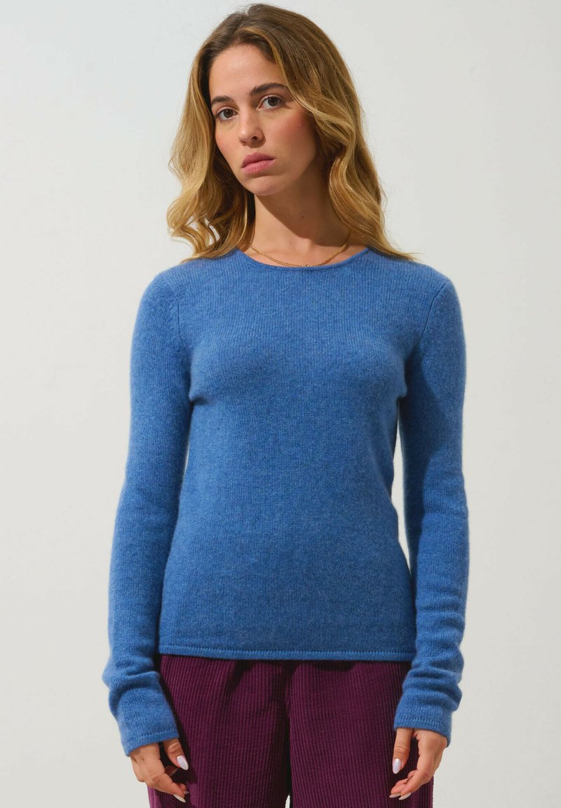 Hellblauer, taillierter Pullover aus weichem, strukturiertem Stoff mit langen Ärmeln und rundem Ausschnitt, kombiniert mit lila Cordhosen.