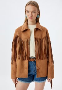 Bruine neplederen suede jas met lange franjes langs de schouders. De jas heeft een knoopsluiting en een klassieke kraag.