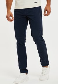 Marineblaue Baumwollchinos mit geradem Schnitt, die eine glatte Textur und klare Linien aufweisen. Kombiniert mit weißen Sneakern für einen Kontrast.