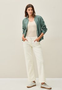 Grön bomberjacka med ribbade ärmar, beige linne, vita vida byxor med subtil textur, och grå sneakers med ljusa accenter.