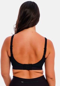 Sort sports-bh med justerbare stropper, mesh-design og lukning med tre hægter bagpå. Glat tekstur med en minimalistisk stil.