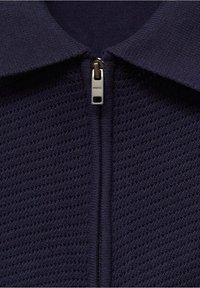 Tissu tricoté texturé bleu marine avec fermeture éclair, doté d'un col avec col et de panneaux lisses contrastants de chaque côté de la fermeture éclair.