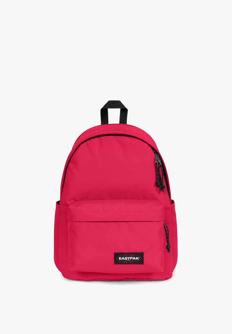 Rosa tygryggsäck med rundad form, framficka, svarta dragkedjor, strukturerad yta och ett handtag på toppen. Logotypen visas tydligt.