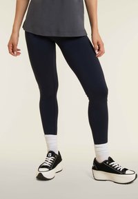 Leggings blu navy con un design aderente, tessuto morbido e cuciture laterali discrete, abbinati a sneakers nere con suola e lacci bianchi.