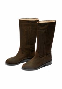 Botas altas de ante marrón con un acabado suave, punta redondeada, suela plana y costuras decorativas en el caña.